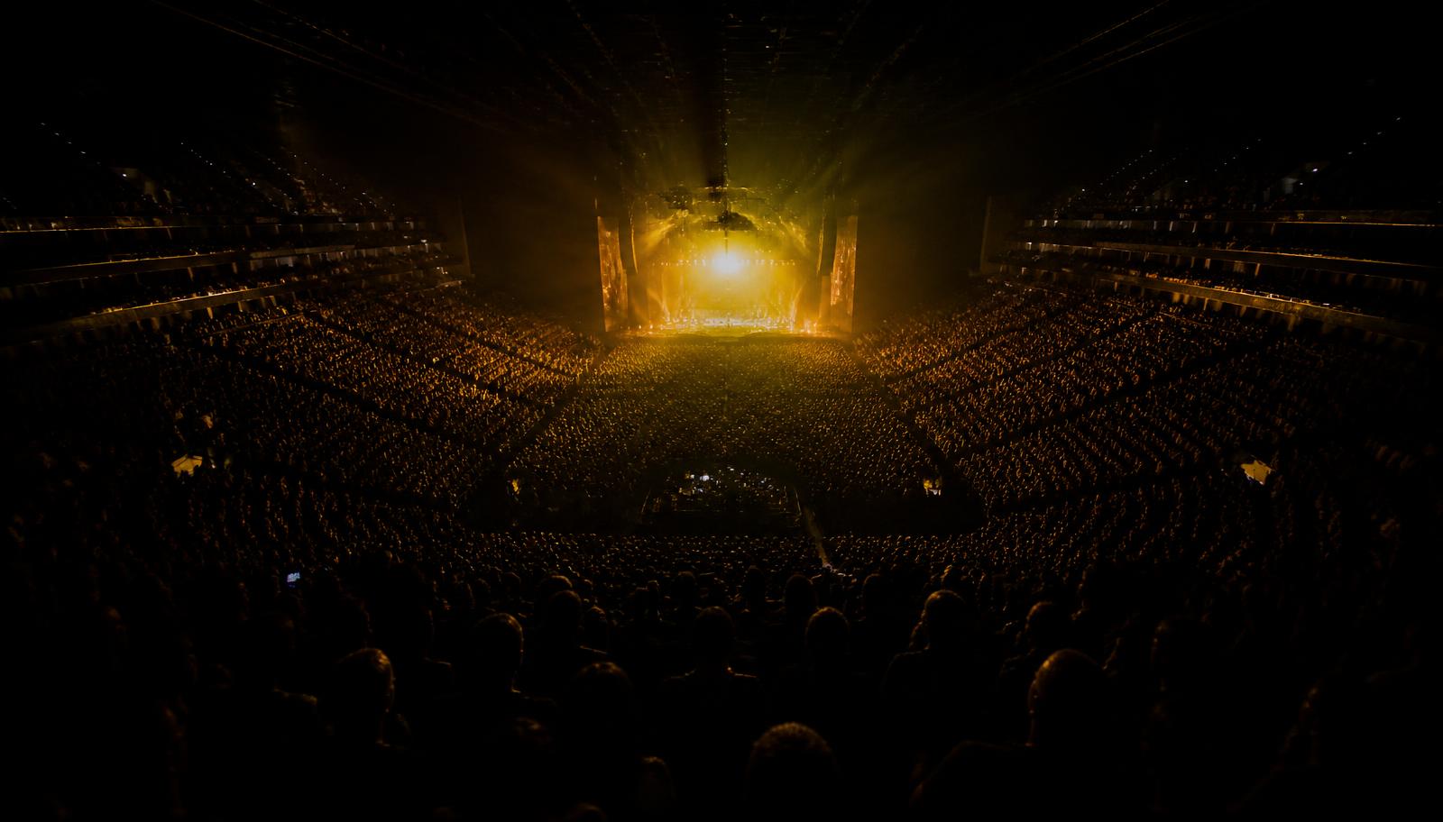 Packed crowd at Hertz Arena during a concert with golden stage lighting